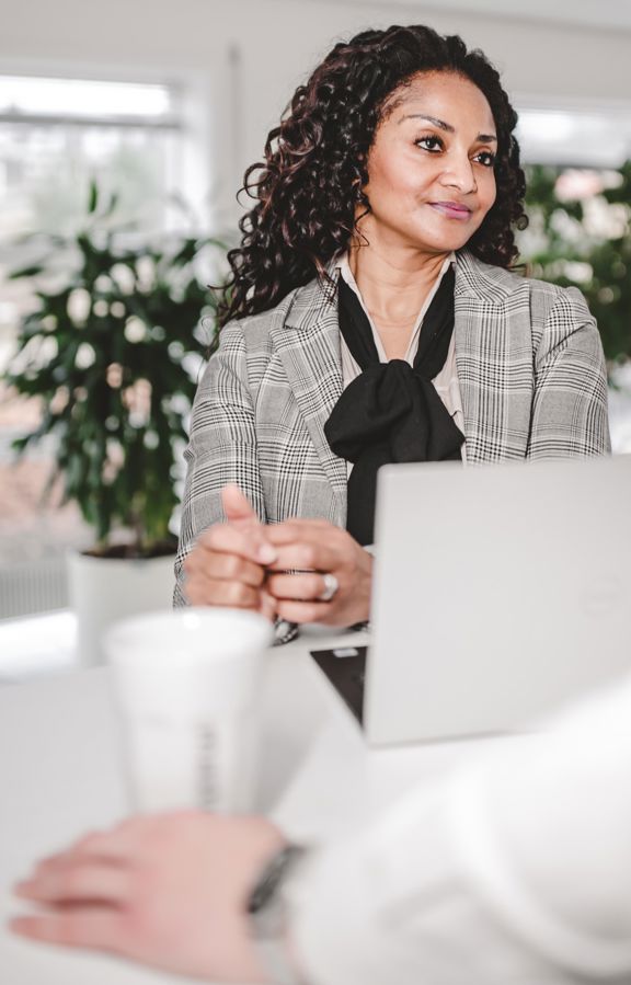 Businesswoman standing in front of a laptop, attentively listening to her colleagues during a meeting.
