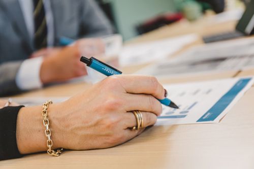 Close-up of a professional's hand holding a Master-branded pen, analyzing a document with graphs during a business meeting.